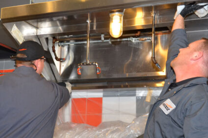 Technician wiping a kitchen hood clean to prevent holiday fire hazards