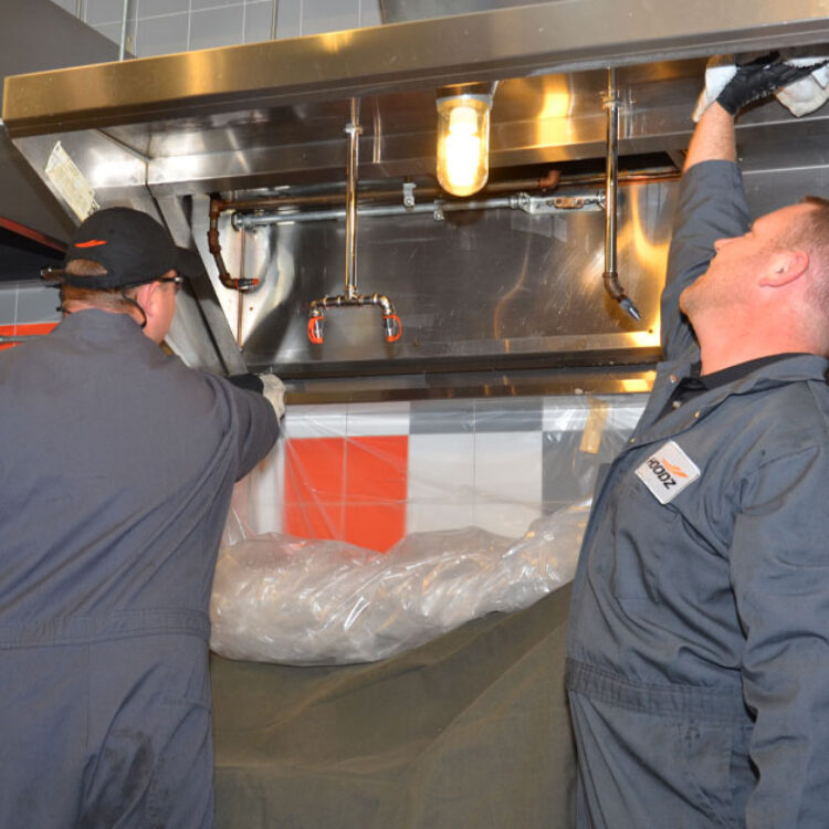 Technician wiping a kitchen hood clean to prevent holiday fire hazards