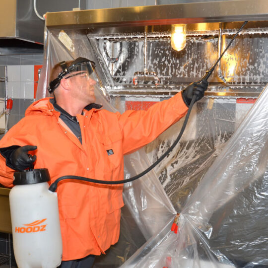 Technician spraying cleaning solution on kitchen exhaust hood