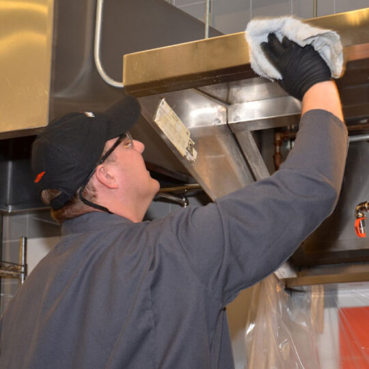 Technician wiping a commercial kitchen hood clean with a towel